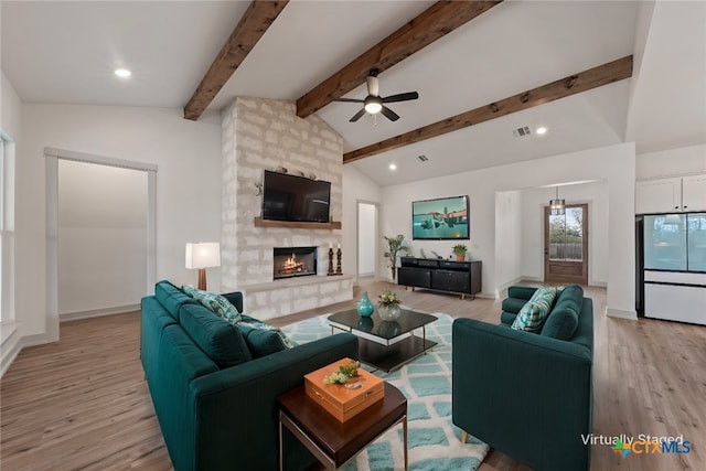 living area with vaulted ceiling with beams, visible vents, light wood-style floors, a large fireplace, and baseboards