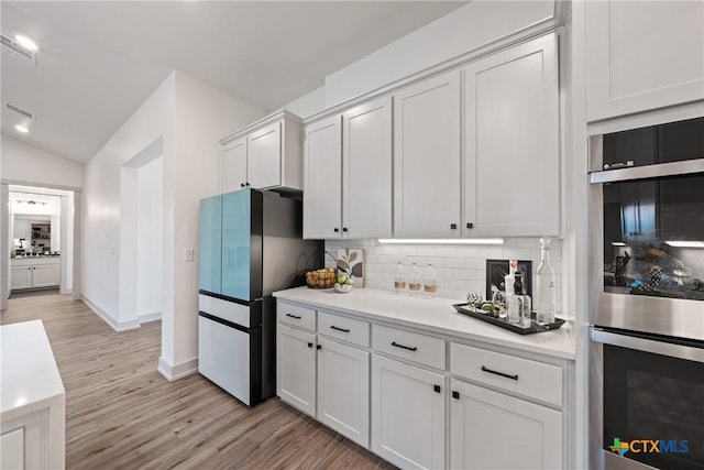 kitchen featuring light wood-style flooring, light countertops, backsplash, and freestanding refrigerator