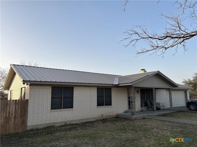 ranch-style home featuring a front lawn, fence, metal roof, a garage, and brick siding