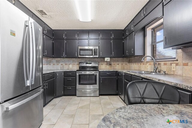 kitchen featuring appliances with stainless steel finishes, tasteful backsplash, sink, light tile patterned floors, and a textured ceiling