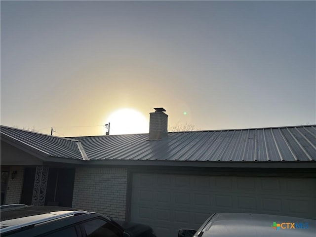 property exterior at dusk featuring a chimney, brick siding, and metal roof