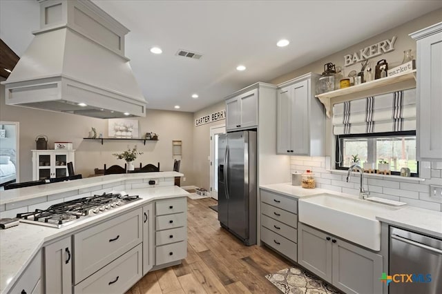 kitchen with custom exhaust hood, decorative backsplash, light wood-type flooring, and stainless steel appliances