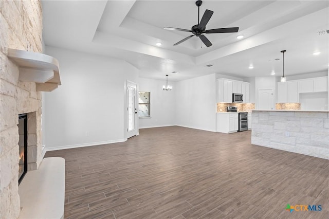 unfurnished living room featuring dark hardwood / wood-style flooring, ceiling fan with notable chandelier, a fireplace, and a raised ceiling