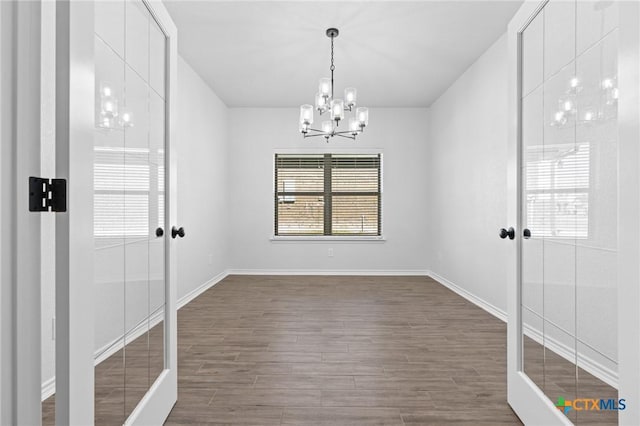 empty room with wood-type flooring and a chandelier