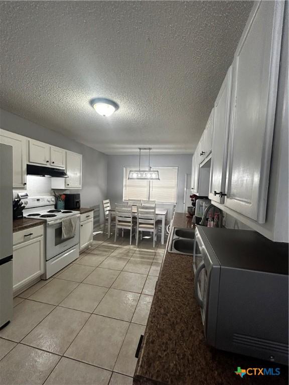 kitchen with dark countertops, light tile patterned flooring, a sink, white appliances, and under cabinet range hood