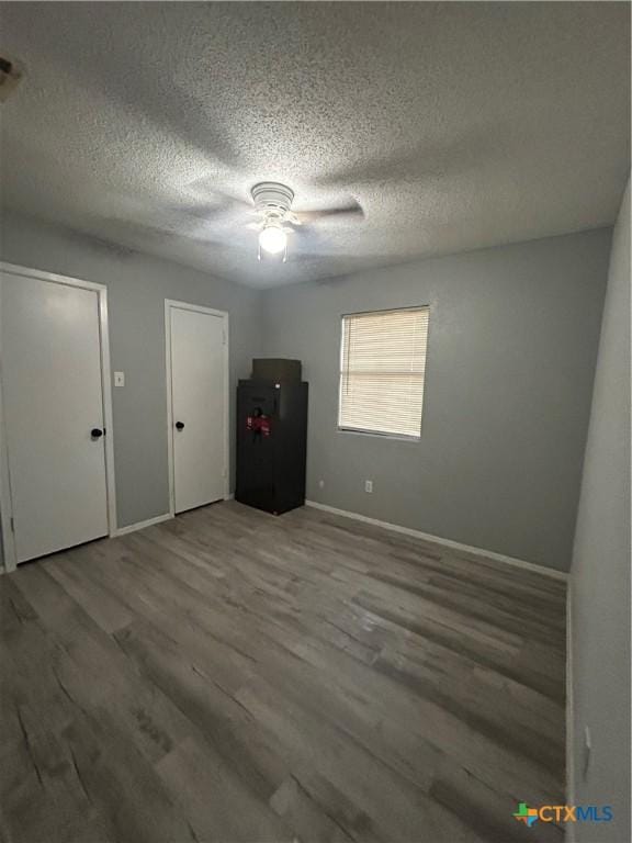 interior space featuring a textured ceiling, two closets, baseboards, and wood finished floors