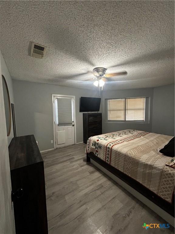 bedroom with ceiling fan, a textured ceiling, visible vents, and wood finished floors