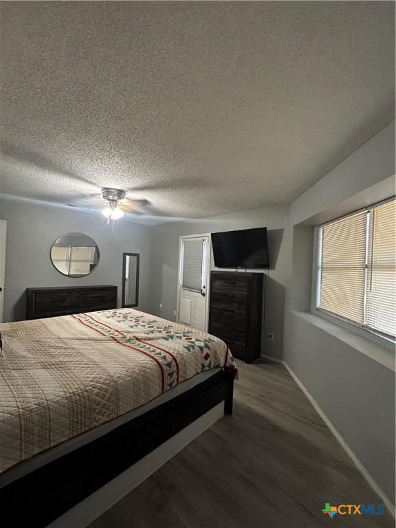 bedroom featuring a ceiling fan, a textured ceiling, baseboards, and wood finished floors