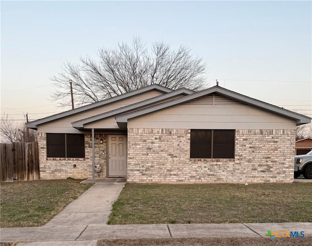 view of front of property featuring fence, a front lawn, and brick siding