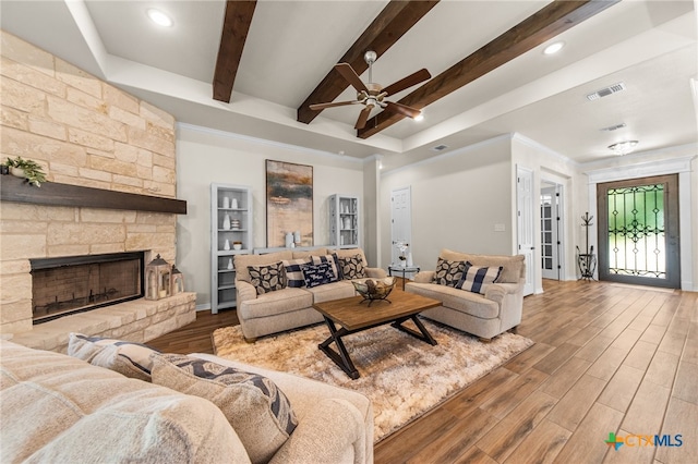 living room with a stone fireplace, wood-type flooring, ceiling fan, and beam ceiling