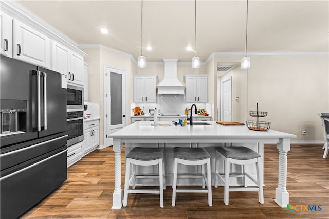 kitchen featuring white cabinetry, appliances with stainless steel finishes, custom range hood, hanging light fixtures, and light hardwood / wood-style flooring