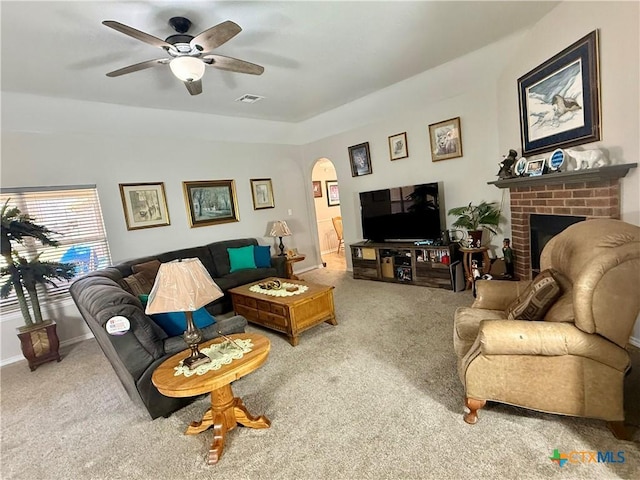 carpeted living room with arched walkways, ceiling fan, visible vents, baseboards, and a brick fireplace