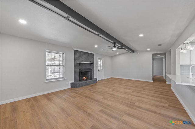 unfurnished living room featuring a brick fireplace, ceiling fan with notable chandelier, lofted ceiling with beams, and light hardwood / wood-style flooring