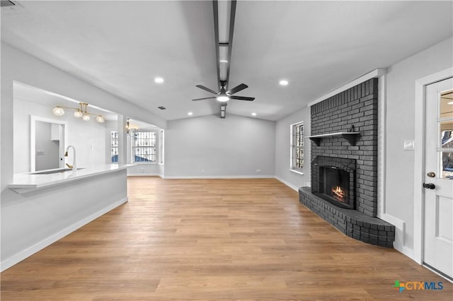 unfurnished living room with sink, a brick fireplace, light hardwood / wood-style flooring, lofted ceiling, and ceiling fan with notable chandelier