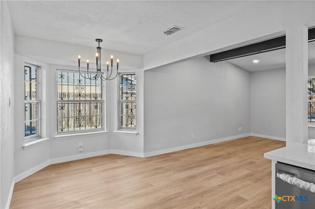 unfurnished dining area with a notable chandelier, light hardwood / wood-style floors, and a textured ceiling