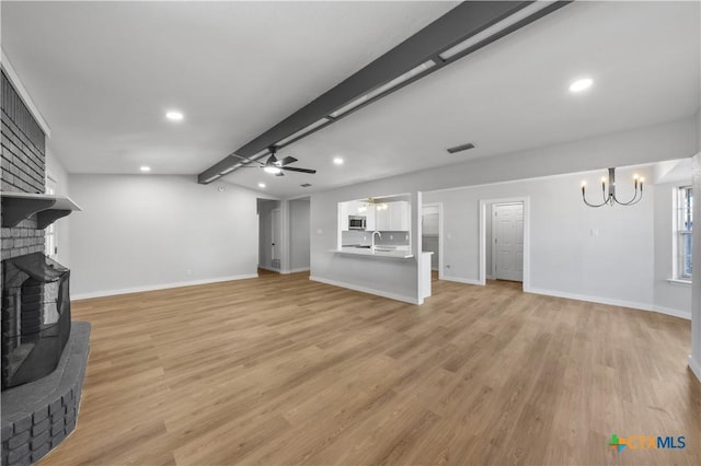 living room featuring a brick fireplace, ceiling fan with notable chandelier, sink, light hardwood / wood-style flooring, and vaulted ceiling with beams