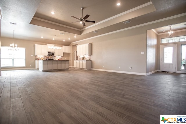 unfurnished living room featuring dark hardwood / wood-style floors, ceiling fan with notable chandelier, crown molding, and a tray ceiling