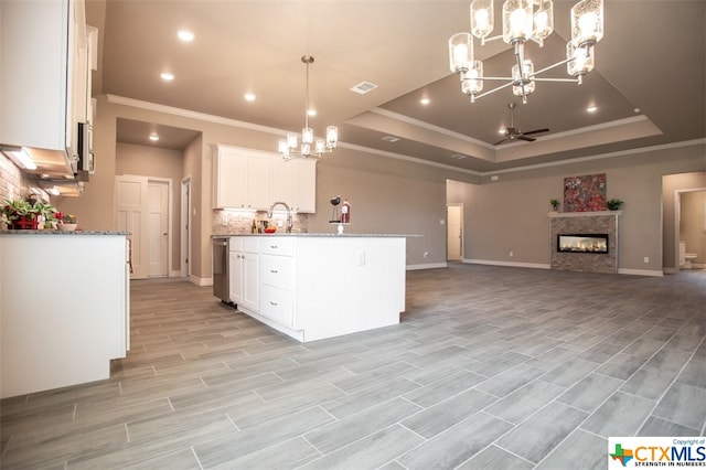 kitchen featuring ceiling fan with notable chandelier, light wood-type flooring, pendant lighting, white cabinets, and a kitchen island with sink