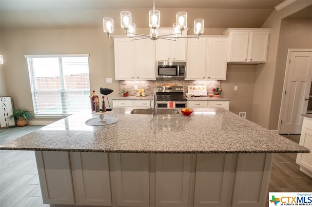 kitchen featuring a center island with sink, sink, light stone counters, appliances with stainless steel finishes, and hardwood / wood-style floors