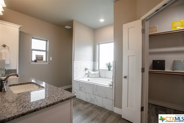 bathroom with hardwood / wood-style floors, vanity, and a relaxing tiled tub