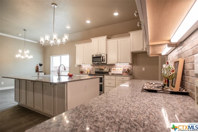 kitchen with appliances with stainless steel finishes, light stone counters, an island with sink, crown molding, and white cabinets