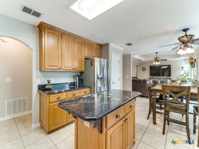 kitchen featuring ceiling fan, light tile patterned floors, dark stone countertops, stainless steel fridge with ice dispenser, and a kitchen island