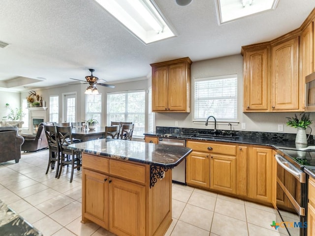 kitchen featuring dark stone counters, sink, ceiling fan, a kitchen island, and stainless steel appliances