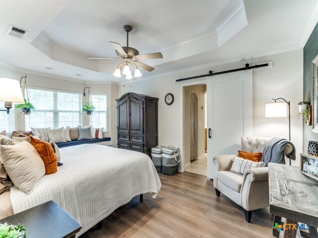 bedroom featuring ceiling fan, a barn door, a raised ceiling, and wood-type flooring