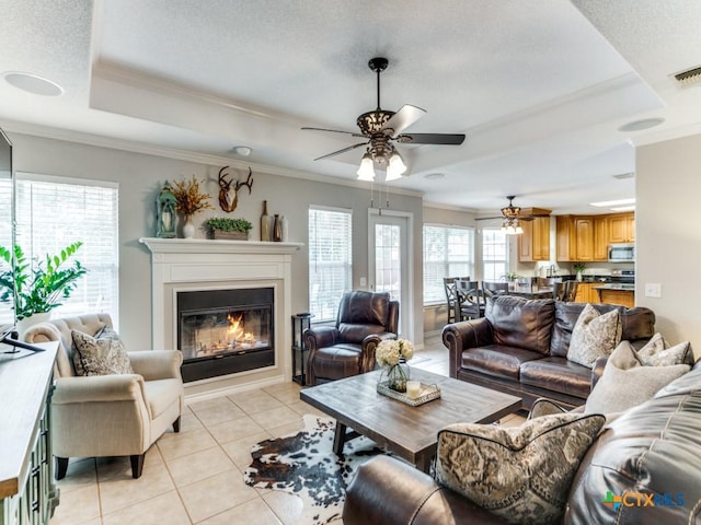 living room with ceiling fan, light tile patterned floors, crown molding, and a tray ceiling