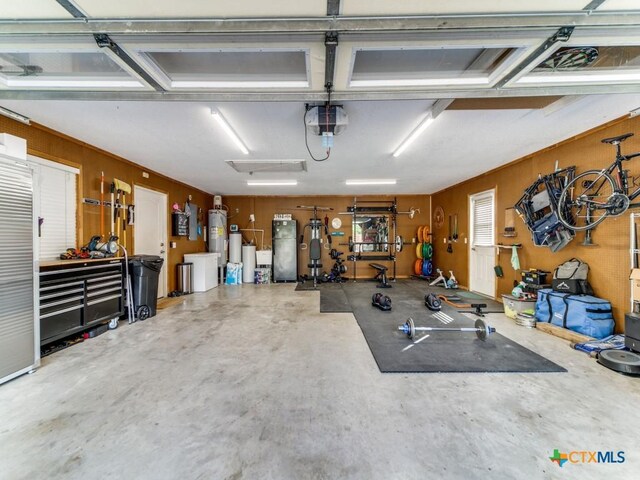 garage featuring a workshop area, wooden walls, a garage door opener, and water heater