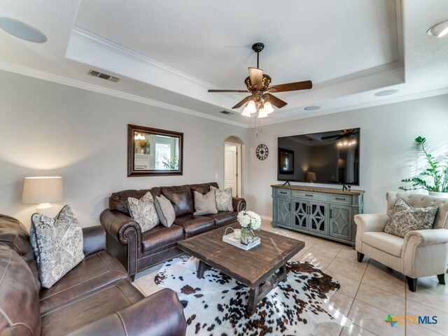 living room with a raised ceiling, crown molding, light tile patterned flooring, and ceiling fan