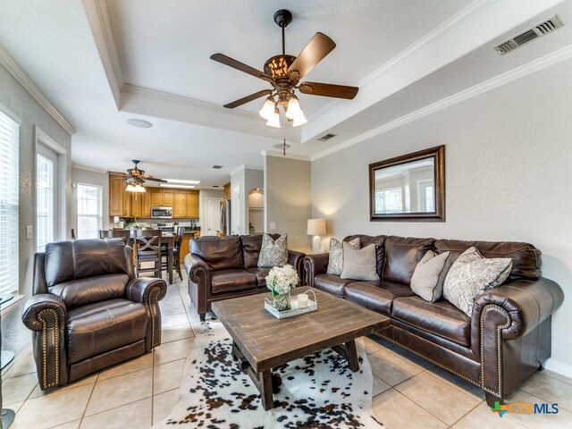 living room featuring ceiling fan, light tile patterned floors, ornamental molding, and a tray ceiling