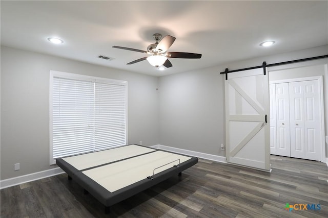 bedroom with a barn door, ceiling fan, a closet, and dark wood-type flooring