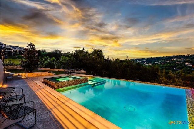 pool at dusk featuring a patio area and an in ground hot tub