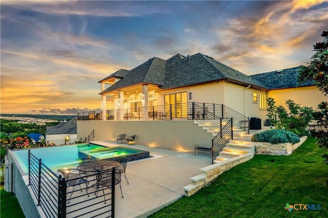 back house at dusk with a patio area, a yard, a swimming pool with hot tub, and central air condition unit