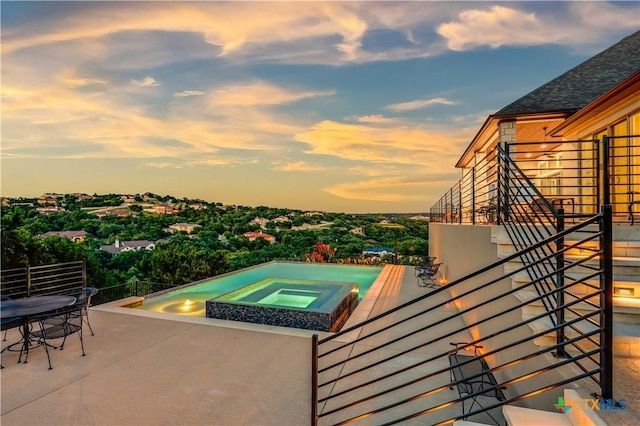 pool at dusk featuring a patio area and an in ground hot tub