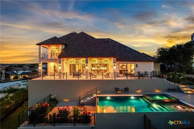 back house at dusk with a pool with hot tub, a balcony, and a patio