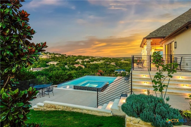 pool at dusk with an in ground hot tub and a patio area