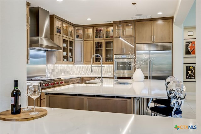 kitchen featuring tasteful backsplash, pendant lighting, a breakfast bar, stainless steel built in refrigerator, and wall chimney exhaust hood