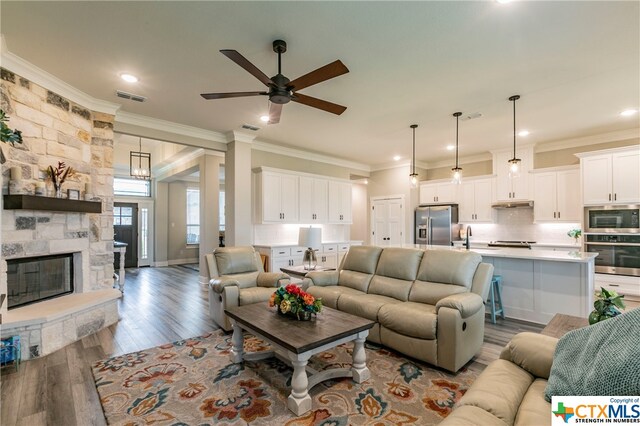 living room with ornamental molding, light hardwood / wood-style flooring, ceiling fan, and a stone fireplace