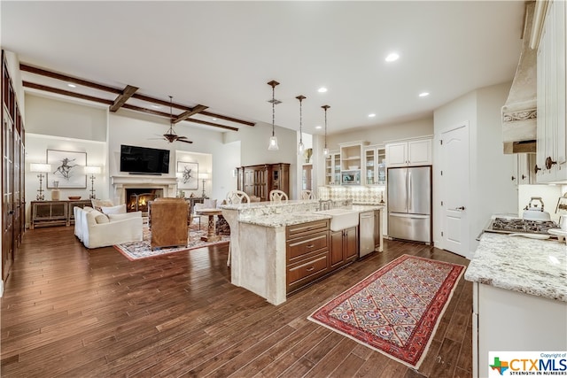 kitchen featuring dark hardwood / wood-style flooring, an island with sink, light stone countertops, pendant lighting, and appliances with stainless steel finishes