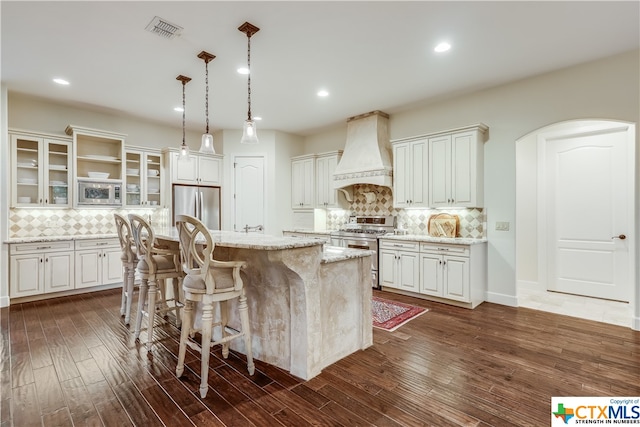 kitchen featuring premium range hood, stainless steel appliances, white cabinetry, dark hardwood / wood-style floors, and a center island