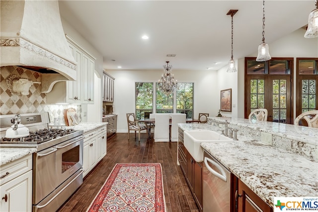 kitchen with sink, appliances with stainless steel finishes, custom range hood, dark wood-type flooring, and pendant lighting