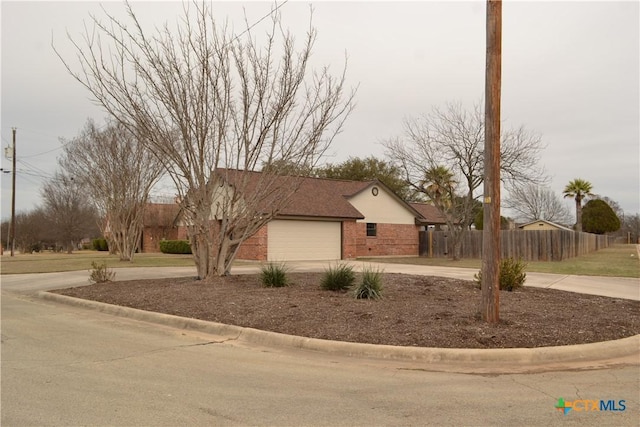 exterior space featuring a garage, concrete driveway, roof with shingles, fence, and brick siding