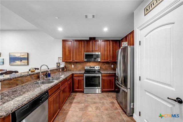 kitchen featuring decorative backsplash, kitchen peninsula, stainless steel appliances, sink, and dark stone countertops