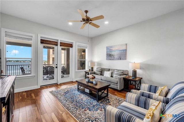 living room with ceiling fan, a water view, and wood-type flooring