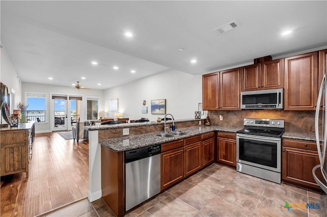 kitchen with french doors, light hardwood / wood-style flooring, kitchen peninsula, dark stone counters, and appliances with stainless steel finishes