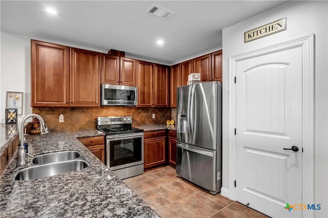 kitchen featuring sink, stainless steel appliances, tasteful backsplash, dark stone counters, and light tile patterned flooring