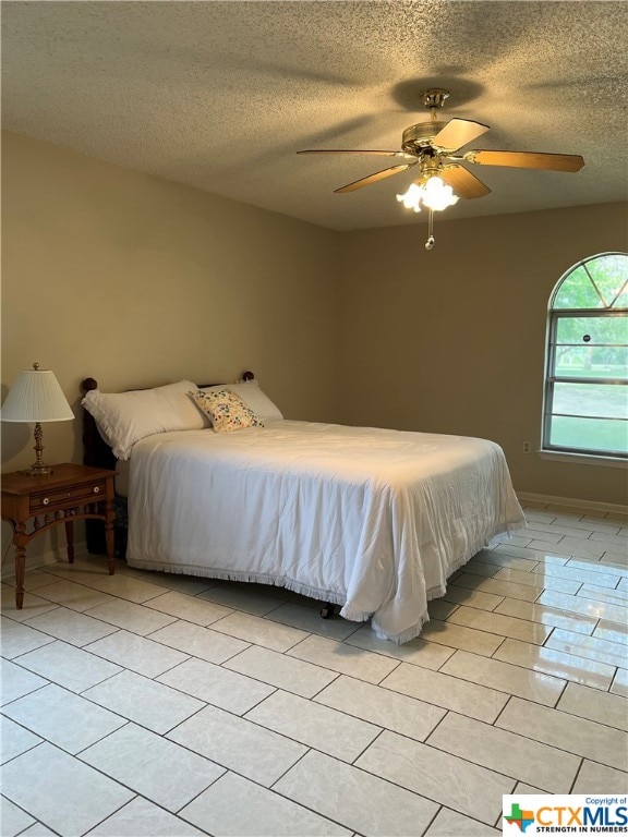 bedroom featuring ceiling fan, light tile patterned floors, and a textured ceiling