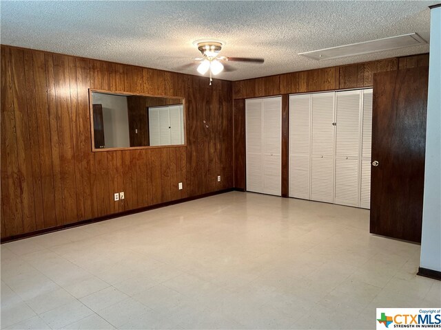 unfurnished bedroom with a textured ceiling, ceiling fan, and wood walls